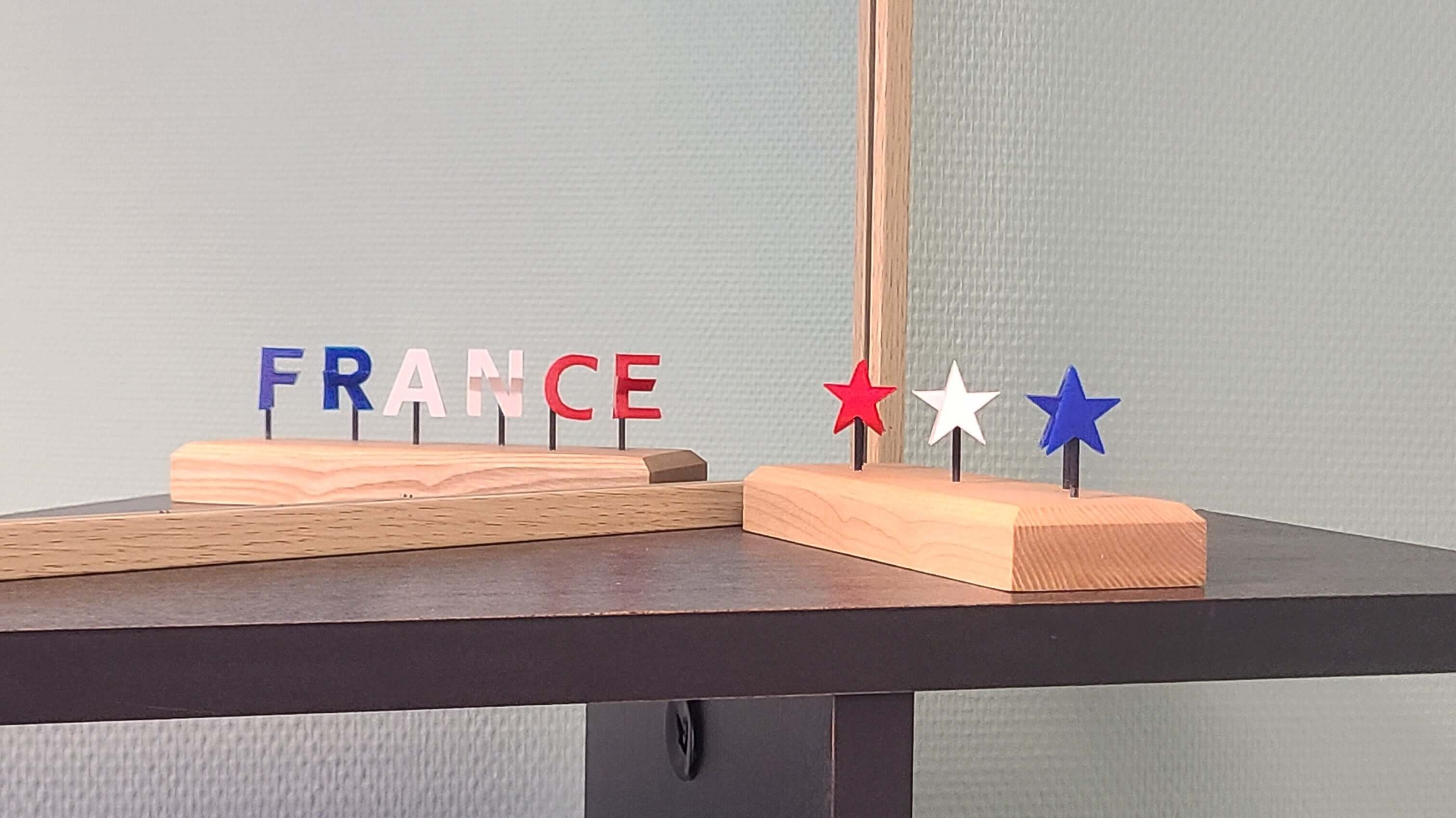 socle en bois surmonté de trois étoiles bleu-blanc-rouges. Quand on le regarde dans le miroir, par illusion d'optique, on voit en tricolore les lettres du mot FRANCE