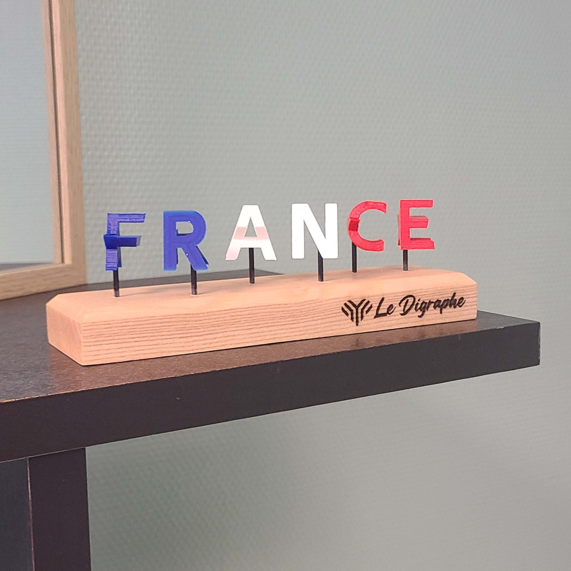 un socle en bois surmonté de lettres tricolores bleu-blanc-rouge formant le mot FRANCE