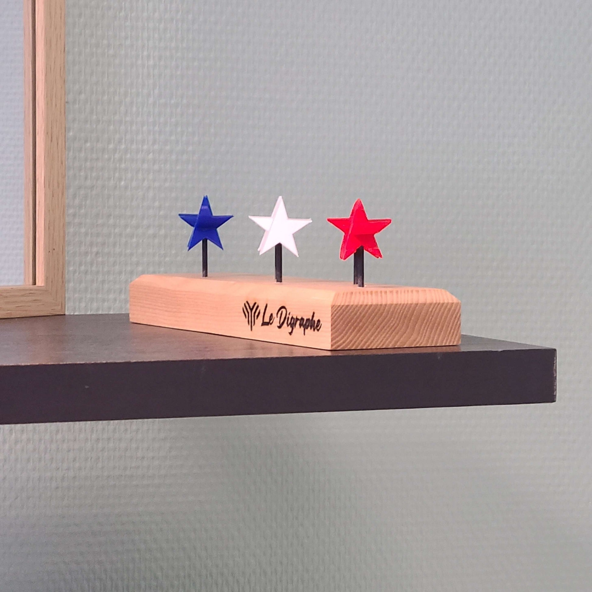 un socle en bois de frêne surmonté de trois étoiles tricolores bleu-blanc-rouge